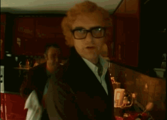 a man wearing glasses is standing in a kitchen with another man