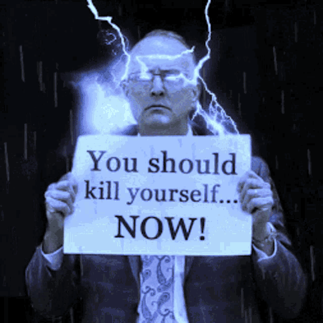 a man in a suit holds up a sign that says you should kill yourself now