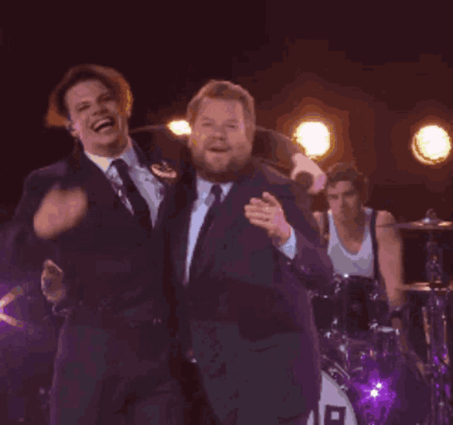 two men are standing next to each other on a stage with a drum set in the background