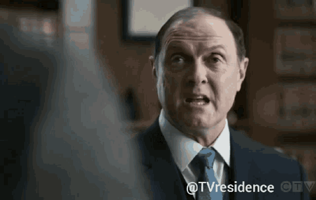 a man in a suit and tie is talking to another man in a room .