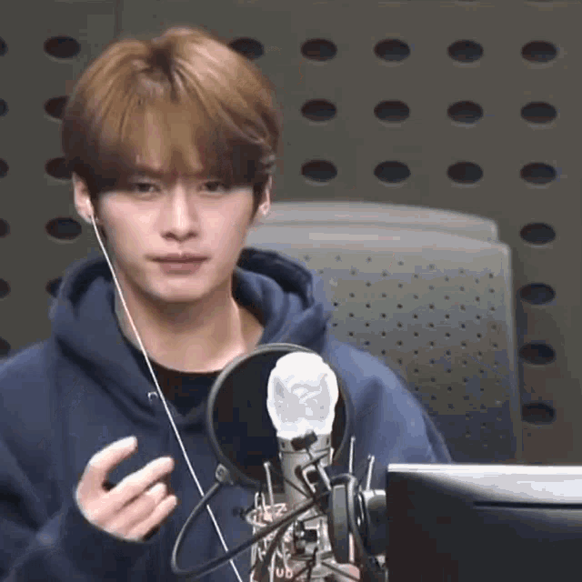a young man is sitting in front of a microphone wearing headphones and a blue hoodie .