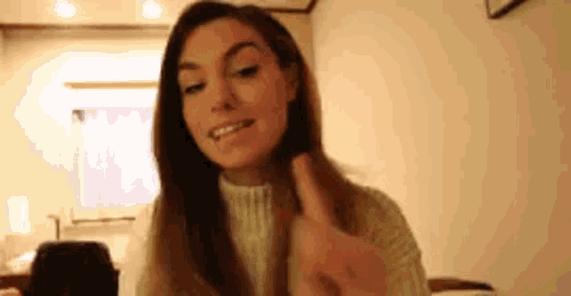 a woman in a white sweater is holding her hair in a room and smiling .