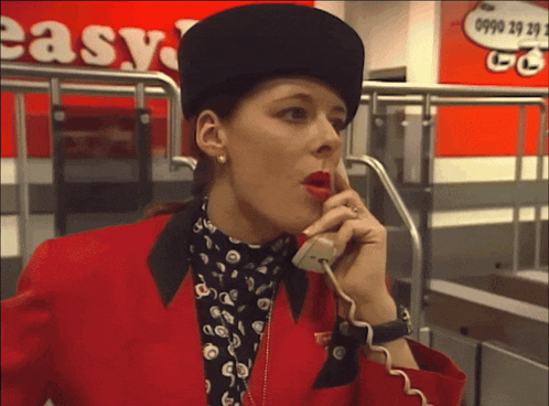 a woman wearing a red jacket and black hat is talking on a phone in front of a sign that says easy