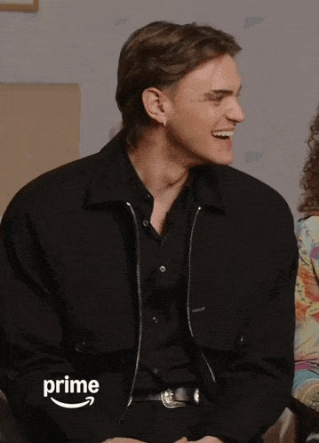 a man in a black jacket is laughing in front of a prime logo