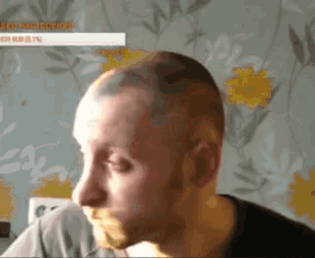 a man with a beard is sitting in front of a flowered wall .