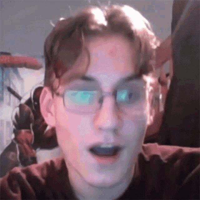 a young man wearing glasses and a red shirt is making a funny face .
