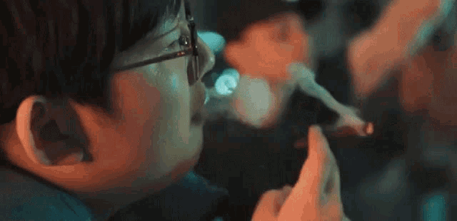 a man with glasses is smoking a cigarette in a dark room .