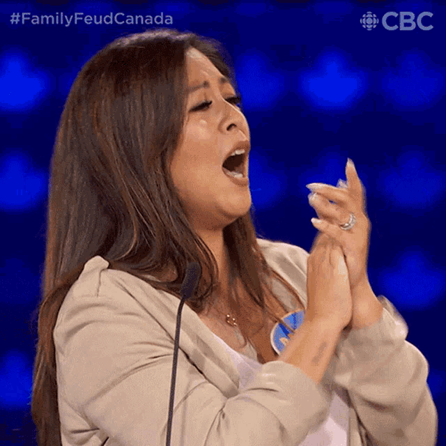a woman claps her hands in front of a microphone with the hashtag familyfeudcanada