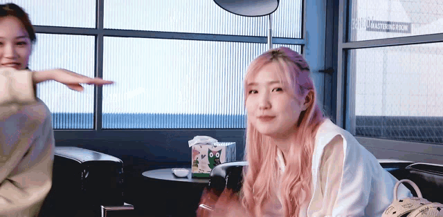 a woman with pink hair is sitting in front of a window with a sign that says ' catering room ' on it .