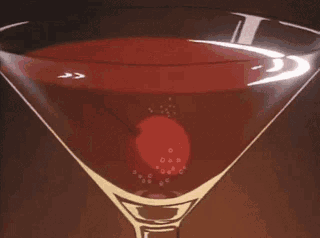 a martini glass with a cherry in it and bubbles coming out of it .