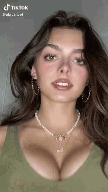 a woman wearing a pearl necklace and hoop earrings has a tiktok sticker on her face