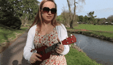 a woman in a floral dress is holding a red ukulele