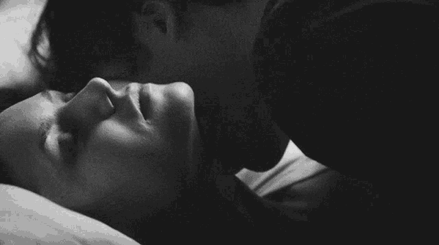 a black and white photo of a man and a woman kissing on a bed .