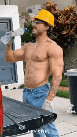 a shirtless construction worker is drinking water from a bottle while standing next to a truck .