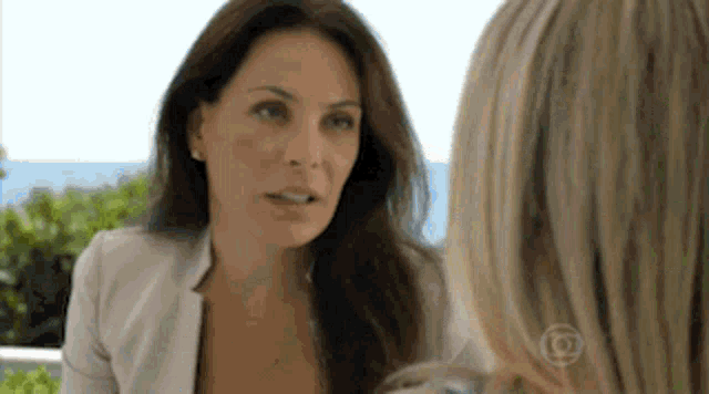 a woman in a white jacket is talking to another woman in front of the ocean ..