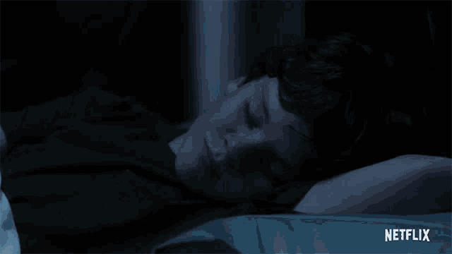 a young boy is sleeping in a dark room with his eyes closed .