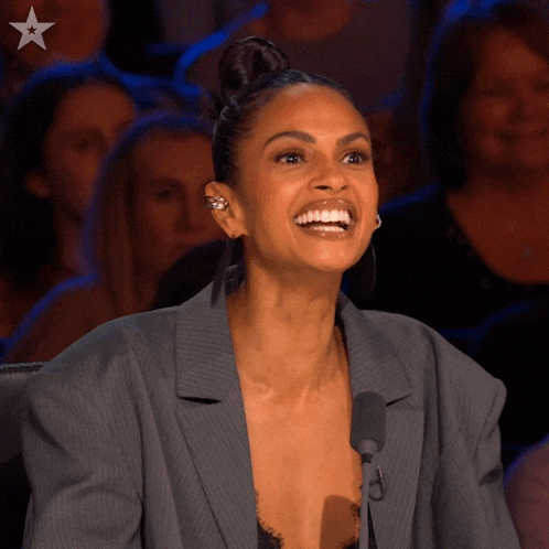 a woman in a suit is smiling while sitting in front of a crowd