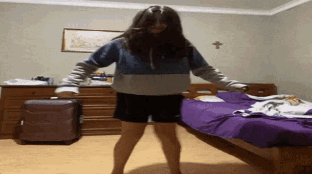 a girl is dancing in a bedroom next to a bed