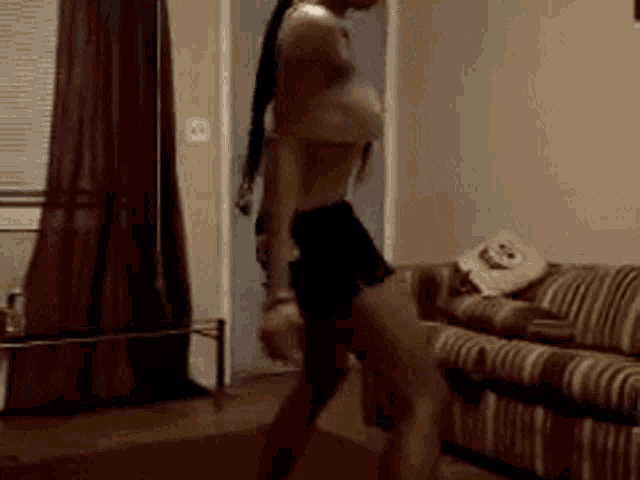 a woman is dancing in a living room with a striped couch .