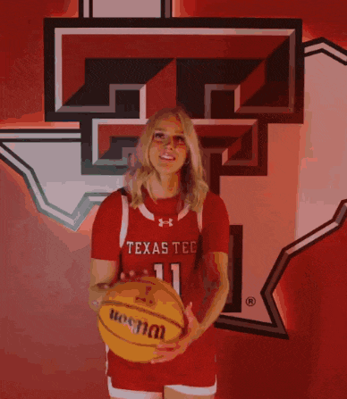 a woman wearing a texas tech jersey stands in front of a texas tech logo