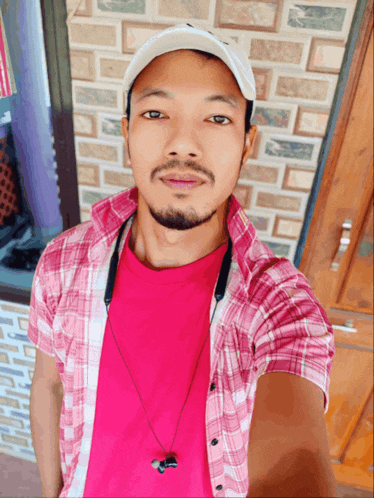 a man wearing a plaid shirt and a baseball cap takes a selfie