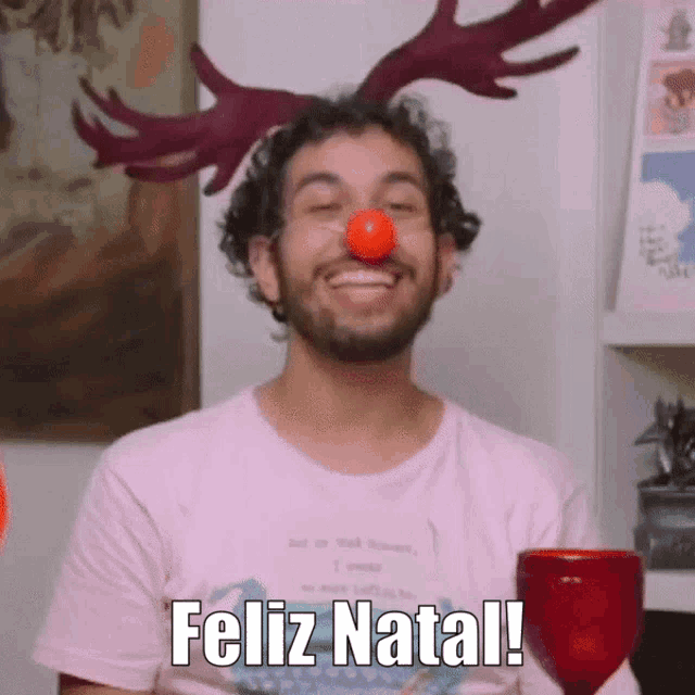 a man with antlers on his head and a red nose has feliz natal written on his shirt