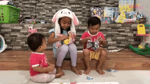 a little girl wearing a bunny hat sits next to a boy and a baby