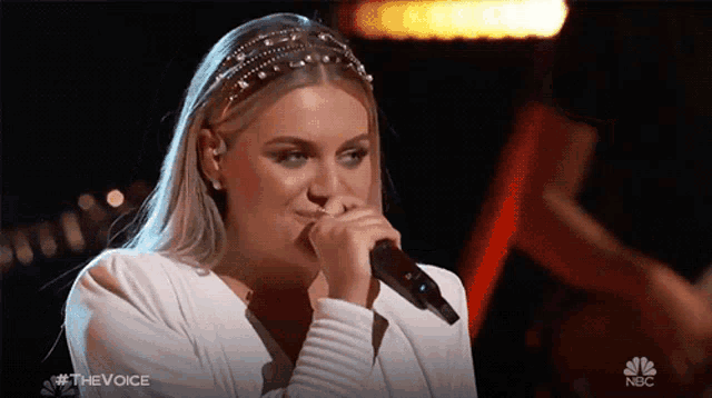 a woman singing into a microphone with the nbc logo in the corner