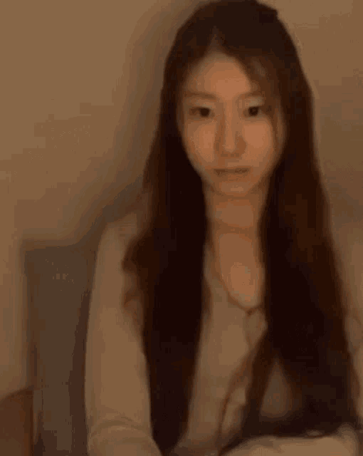 a woman with long brown hair is sitting on a bed looking at the camera .