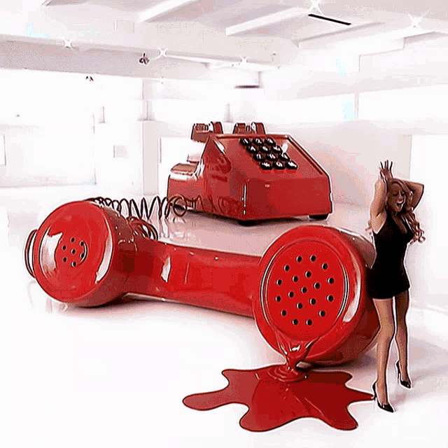 a woman in a black dress stands next to a large red phone