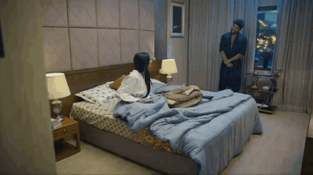 a man in a robe stands next to a woman in a bathrobe on a bed