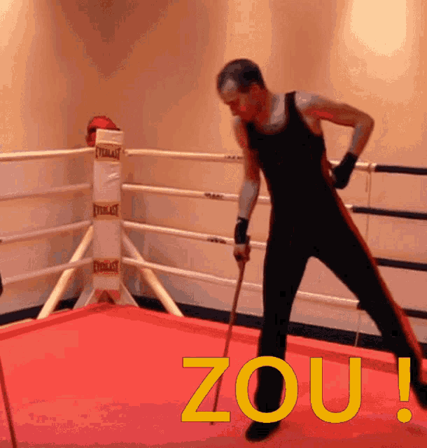 a man in a boxing ring is holding a pool cue and the word zou is on the floor