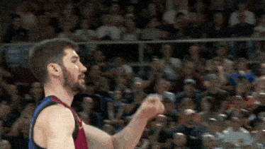 a basketball player is standing in front of a crowd with his fist in the air .
