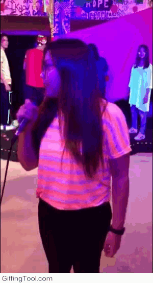a woman singing into a microphone in front of a sign that says hope on it