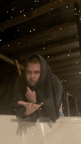 a man in a hooded sweatshirt stands on a white surface