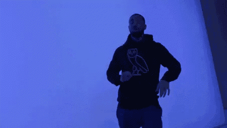 a man wearing a black hoodie with an owl on it is standing in front of a blue wall .