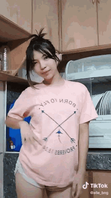 a woman wearing a pink t-shirt with arrows on it is standing in a kitchen