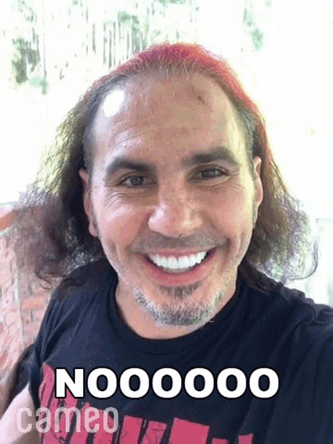 a man with red hair is smiling and wearing a black t-shirt that says nooooo cameo