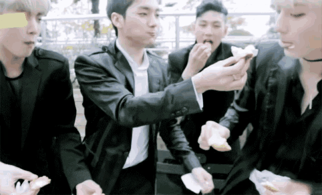 a group of young men in suits are eating food