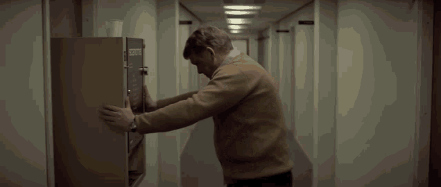 a man in a brown sweater is reaching into a vending machine that says scottie