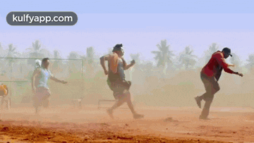 a group of people are running on a dirt field with the words kulfyapp.com on the bottom .