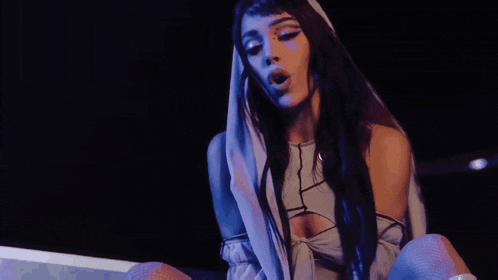 a woman with long black hair and a hood on her head is singing