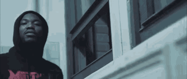 a man wearing a hoodie with the word meth on it stands in front of a window