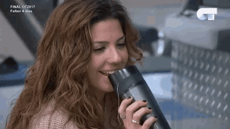 a woman is drinking water from a thermos while wearing headphones .