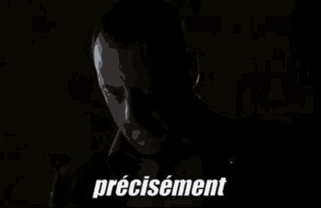 a man in a suit and tie is standing in the dark with the word precisement written on the bottom .