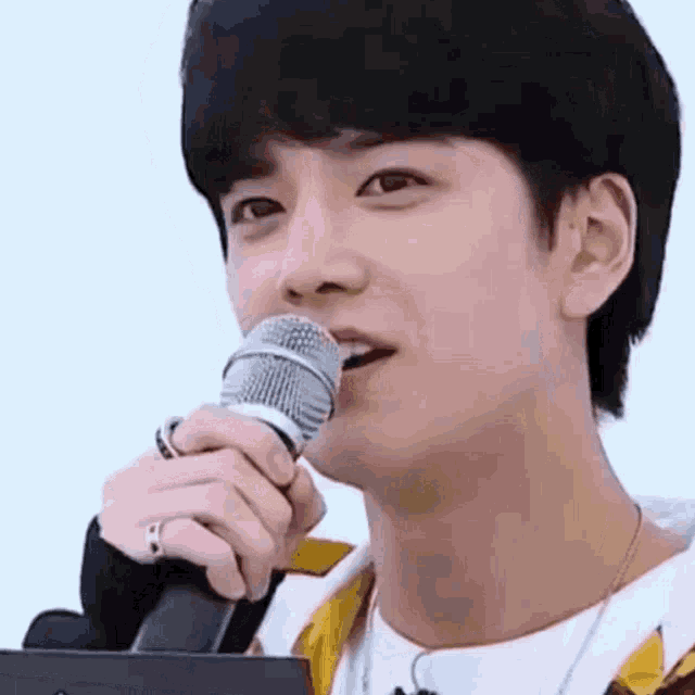 a young man is holding a microphone in front of his mouth .
