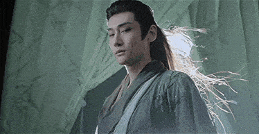 a man with long hair in a kimono is standing in front of a green curtain .