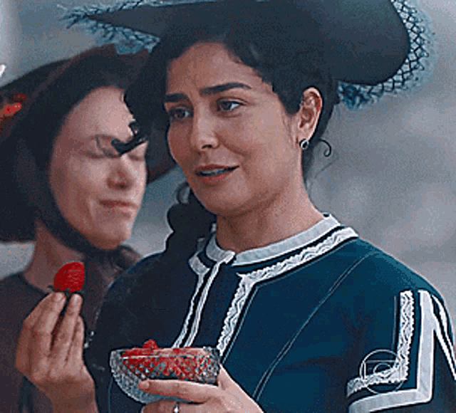 a woman is holding a bowl of strawberries in her hand