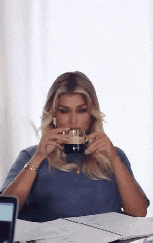 a woman is drinking a cup of coffee while sitting at a table .