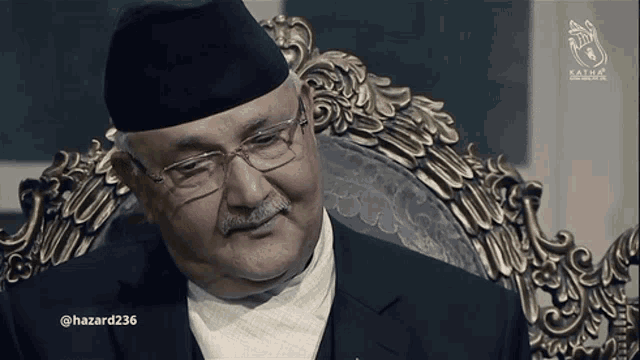 a man with glasses and a mustache sits in a chair with the hashtag hazard236 on the bottom